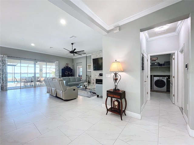 living room with ceiling fan, ornamental molding, a stone fireplace, and washer / dryer