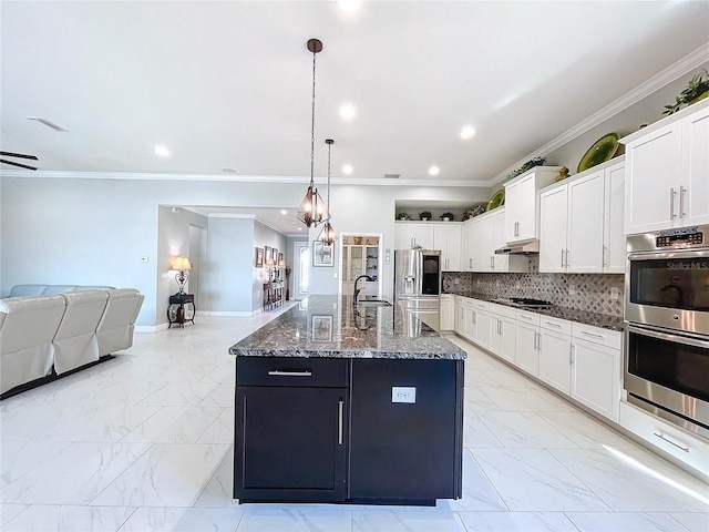 kitchen with white cabinetry, stainless steel appliances, decorative backsplash, a center island with sink, and decorative light fixtures