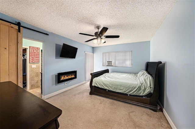 carpeted bedroom with ceiling fan, connected bathroom, a barn door, and a textured ceiling