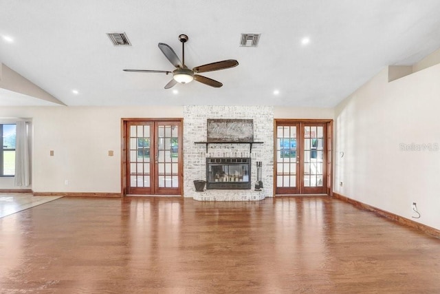 unfurnished living room featuring lofted ceiling, ceiling fan, hardwood / wood-style floors, a brick fireplace, and french doors