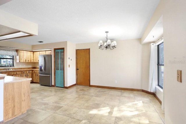 kitchen featuring light brown cabinetry, sink, stainless steel fridge, hanging light fixtures, and an inviting chandelier