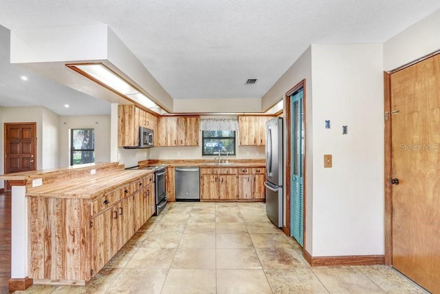 kitchen with sink, kitchen peninsula, a textured ceiling, and appliances with stainless steel finishes