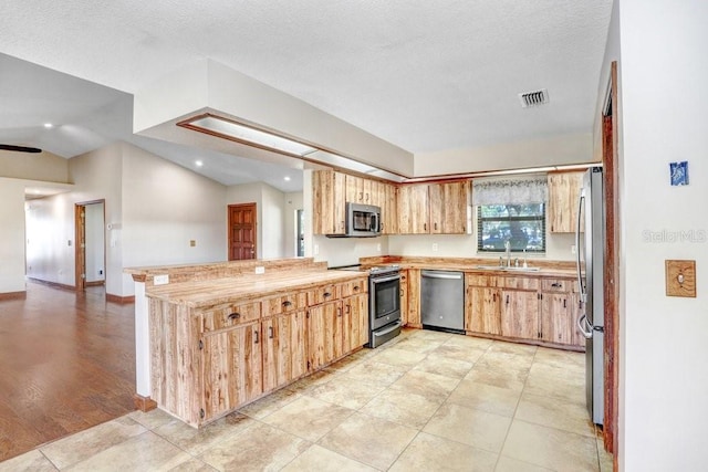 kitchen with sink, vaulted ceiling, light tile patterned floors, appliances with stainless steel finishes, and kitchen peninsula