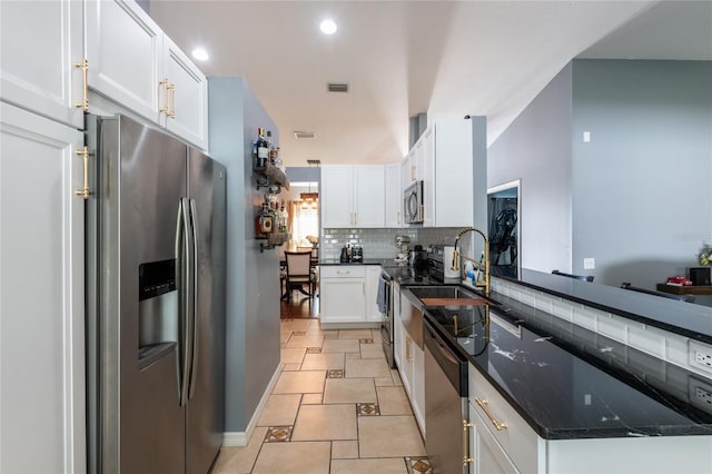 kitchen featuring appliances with stainless steel finishes, tasteful backsplash, white cabinetry, sink, and dark stone countertops