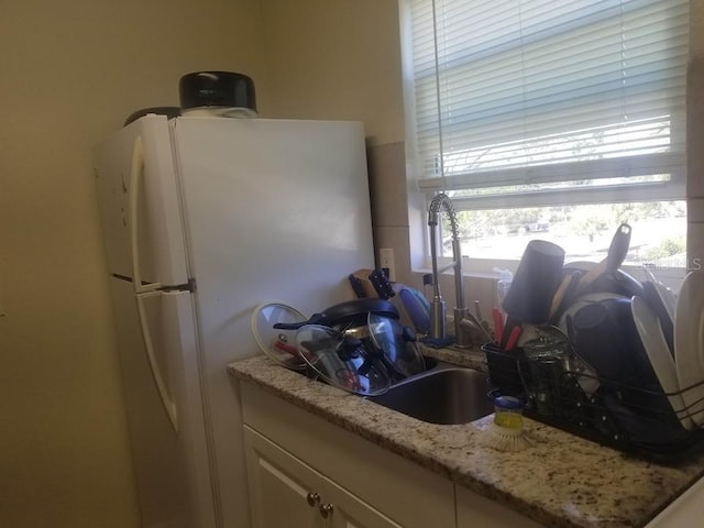 kitchen featuring white cabinetry, white fridge, and light stone counters