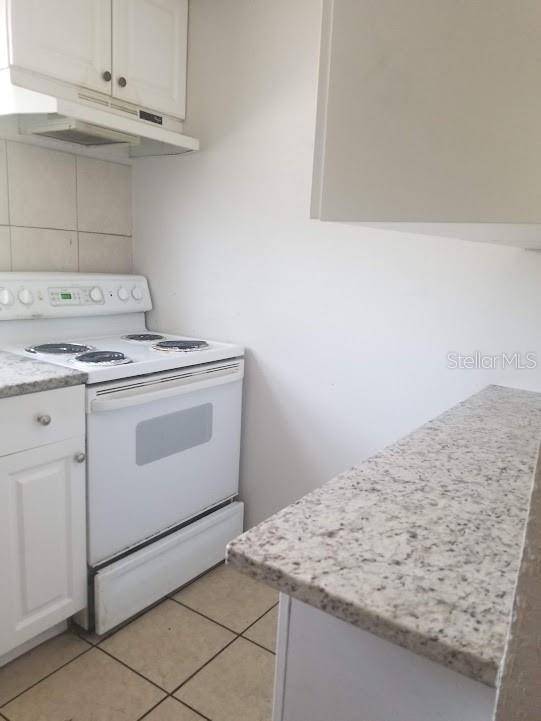 kitchen featuring white electric range oven, white cabinetry, light stone counters, tasteful backsplash, and light tile patterned floors