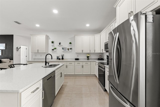 kitchen featuring sink, appliances with stainless steel finishes, light stone countertops, an island with sink, and white cabinets