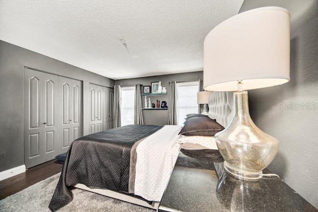 bedroom featuring two closets, dark wood-type flooring, and a textured ceiling