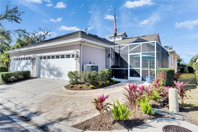 view of side of property featuring stucco siding, an attached garage, central AC unit, glass enclosure, and driveway