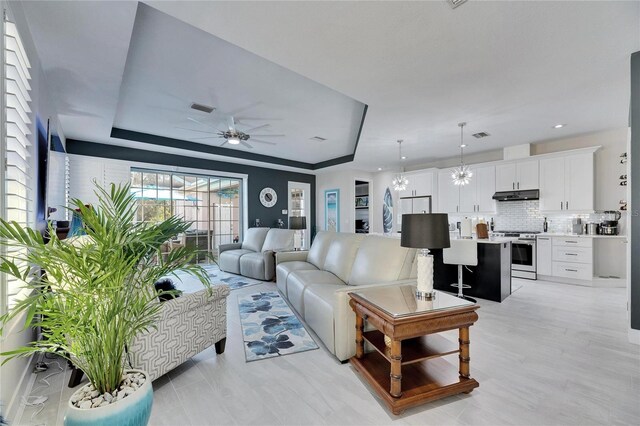 living area featuring ceiling fan with notable chandelier, a raised ceiling, and visible vents