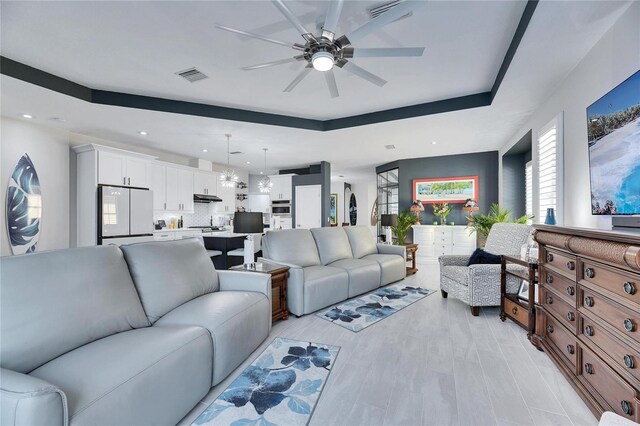 living room featuring ceiling fan, recessed lighting, visible vents, light wood-style floors, and a tray ceiling