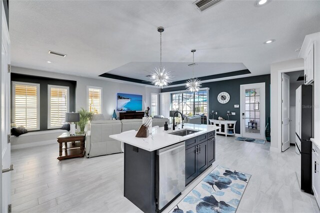 kitchen featuring a center island with sink, a raised ceiling, light countertops, stainless steel dishwasher, and white cabinets