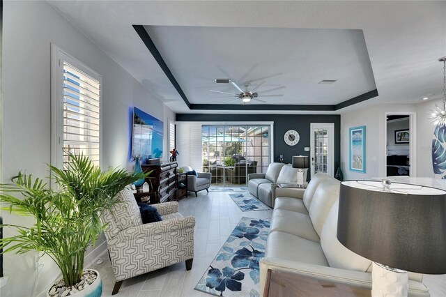 living room featuring plenty of natural light, visible vents, a tray ceiling, and a ceiling fan