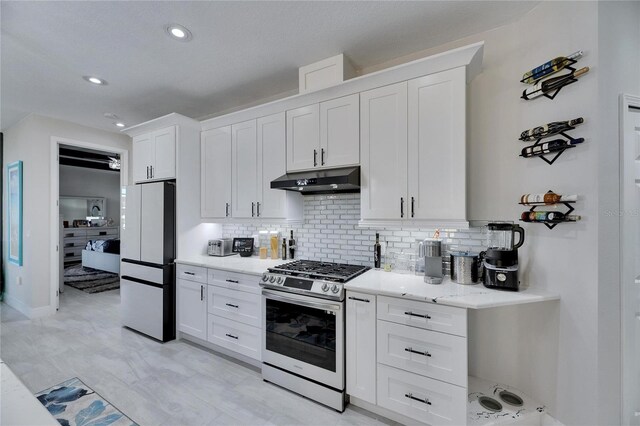 kitchen featuring stainless steel gas range oven, white refrigerator, and white cabinetry