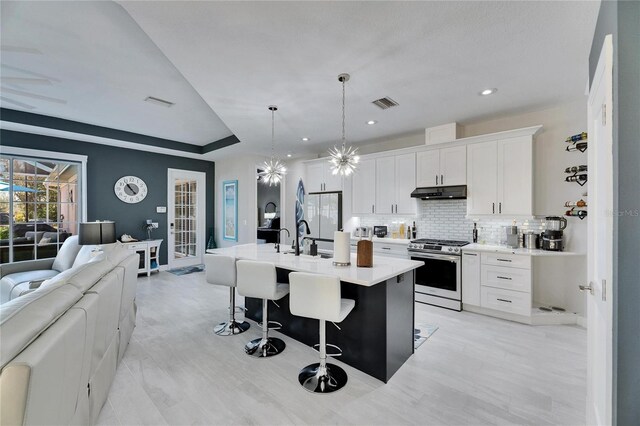 kitchen featuring white cabinets, open floor plan, hanging light fixtures, stainless steel gas range, and light countertops