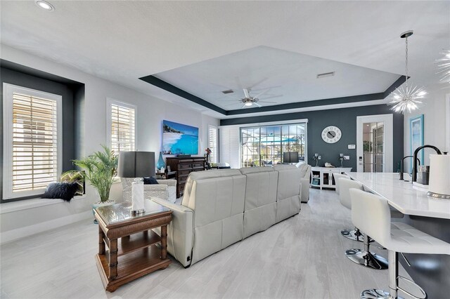 living room featuring ceiling fan, visible vents, light wood-style floors, baseboards, and a raised ceiling