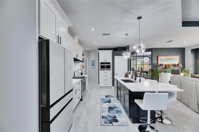 kitchen with pendant lighting, stainless steel appliances, open floor plan, white cabinets, and an island with sink