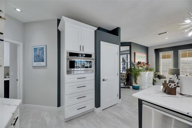 kitchen with visible vents, baseboards, stainless steel oven, white cabinets, and light stone countertops