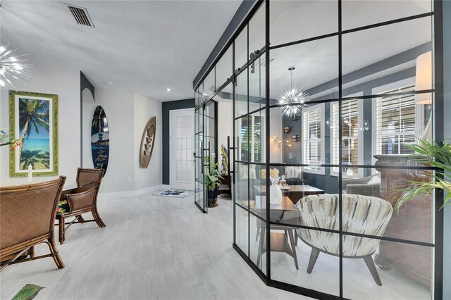 hall featuring arched walkways, a notable chandelier, visible vents, light wood-style floors, and baseboards