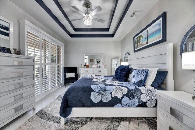 bedroom with a tray ceiling, visible vents, and a ceiling fan