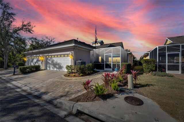 view of front facade featuring glass enclosure, central air condition unit, decorative driveway, stucco siding, and a front yard