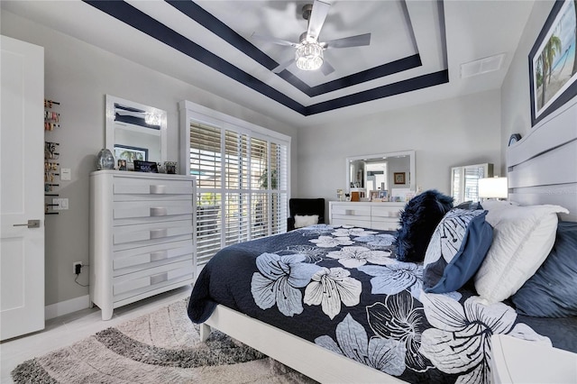 bedroom with ceiling fan, a tray ceiling, visible vents, and baseboards