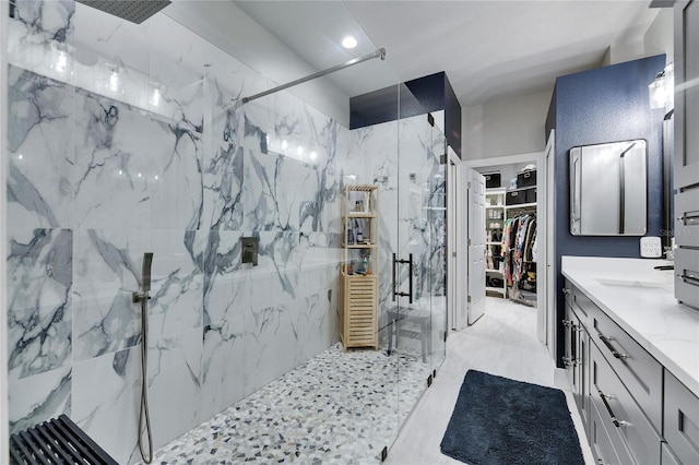 bathroom featuring a walk in closet, vanity, and a marble finish shower