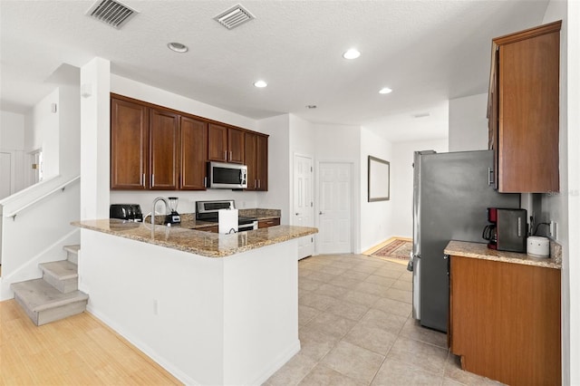 kitchen with light stone counters, sink, stainless steel appliances, and kitchen peninsula