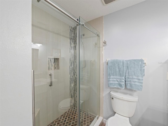 bathroom with toilet, a shower with door, and a textured ceiling