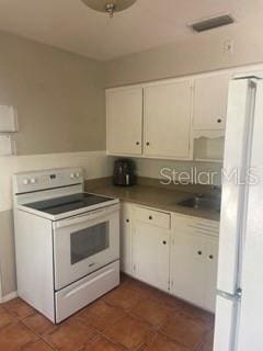 kitchen featuring dark tile patterned floors, white cabinets, and white appliances