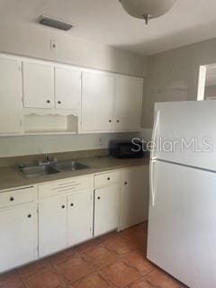 kitchen with white refrigerator, sink, white cabinets, and dark tile patterned floors