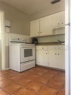 kitchen with white electric range, dark tile patterned flooring, sink, and white cabinets