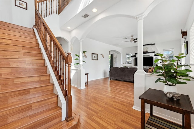 foyer entrance featuring ceiling fan, arched walkways, visible vents, light wood-style floors, and ornate columns