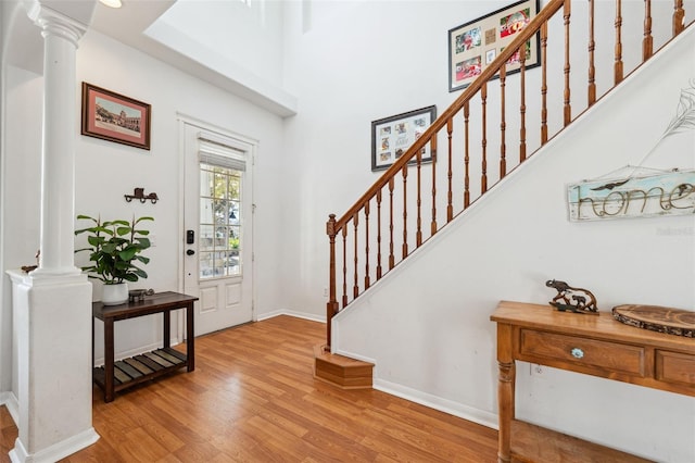 foyer entrance with baseboards, light wood-style floors, a high ceiling, stairs, and ornate columns