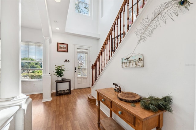 foyer entrance with decorative columns, a towering ceiling, wood finished floors, baseboards, and stairs