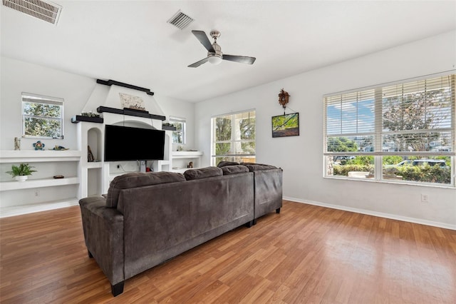 living area featuring a ceiling fan, visible vents, baseboards, and wood finished floors