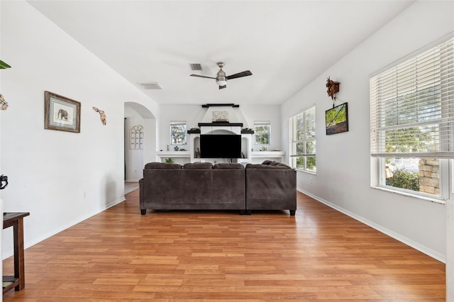 living area featuring arched walkways, visible vents, ceiling fan, and light wood finished floors