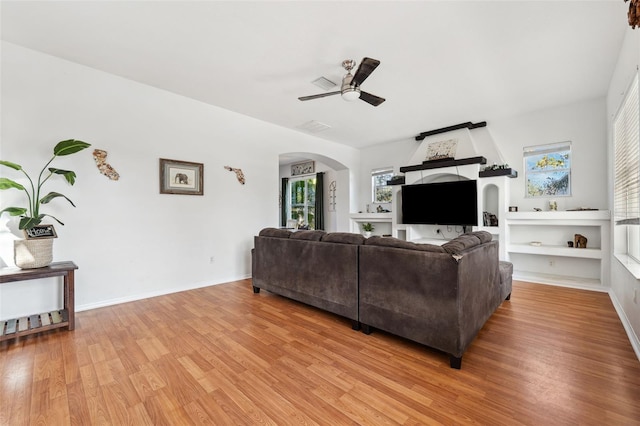 living room with light wood finished floors, ceiling fan, arched walkways, and baseboards