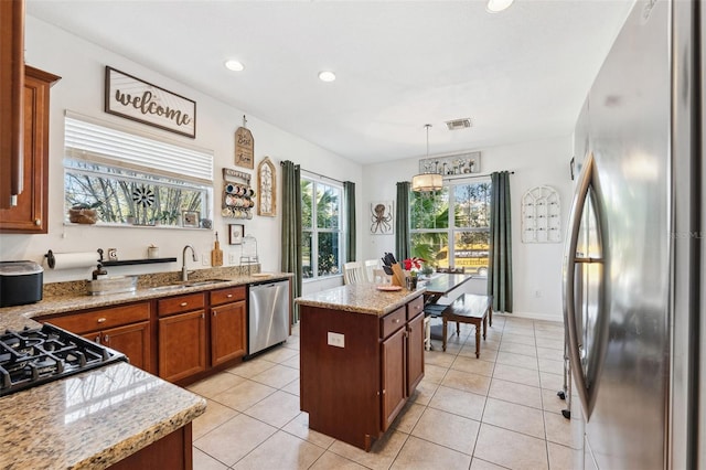 kitchen with a center island, decorative light fixtures, appliances with stainless steel finishes, brown cabinetry, and a sink