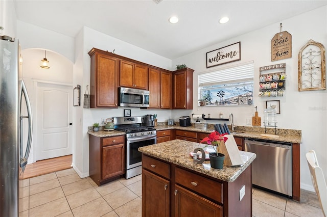 kitchen with a center island, arched walkways, appliances with stainless steel finishes, light tile patterned flooring, and light stone countertops