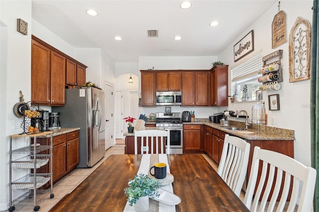 kitchen with light stone counters, stainless steel appliances, a sink, visible vents, and brown cabinets