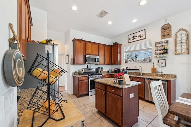 kitchen with stainless steel appliances, a sink, visible vents, a center island, and light stone countertops