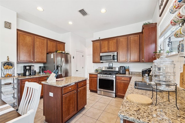 kitchen featuring stainless steel appliances, visible vents, a kitchen island, and light stone countertops