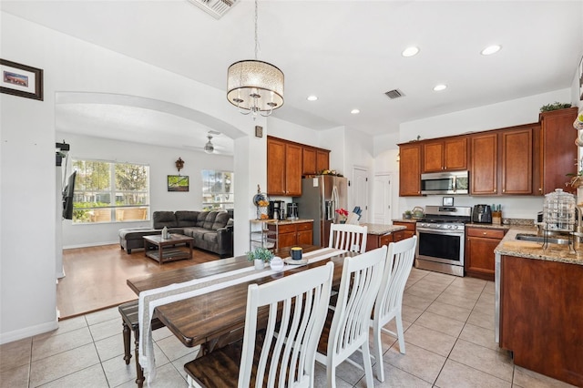 kitchen with arched walkways, light stone counters, stainless steel appliances, open floor plan, and decorative light fixtures