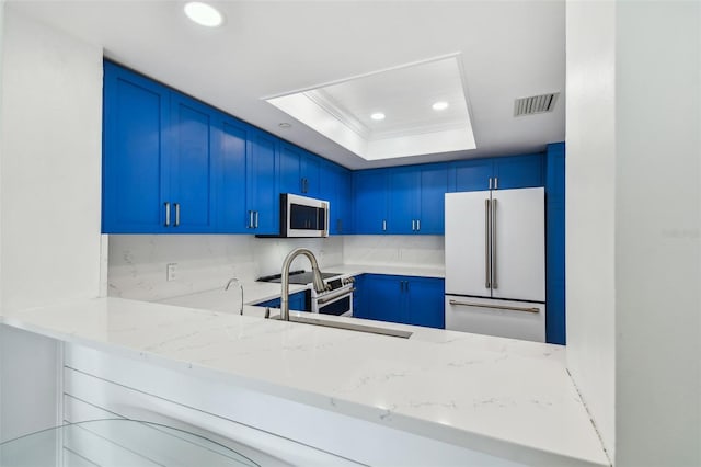 kitchen featuring high quality appliances, blue cabinetry, light stone counters, and a tray ceiling