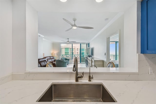 kitchen with sink, ornamental molding, ceiling fan, and light stone countertops