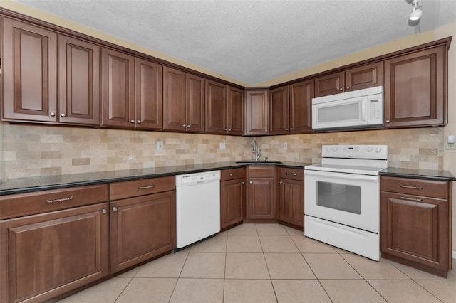 kitchen with light tile patterned flooring, sink, dark stone counters, decorative backsplash, and white appliances