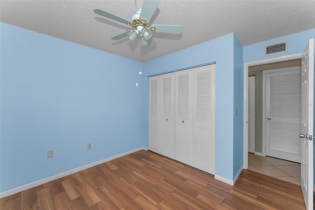 unfurnished bedroom with ceiling fan, hardwood / wood-style floors, a textured ceiling, and a closet