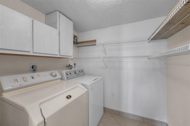 laundry area with cabinets, separate washer and dryer, a textured ceiling, and light tile patterned floors