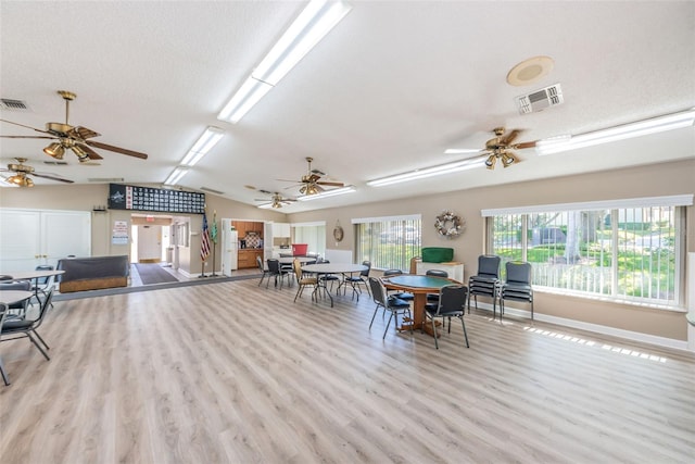 dining area with vaulted ceiling, a textured ceiling, and light hardwood / wood-style flooring